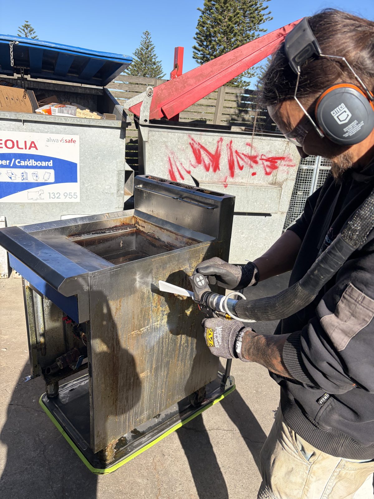 Dry ice blasting nozzle working the fryer cabinet side, CO2 vapour visible, grease lifting