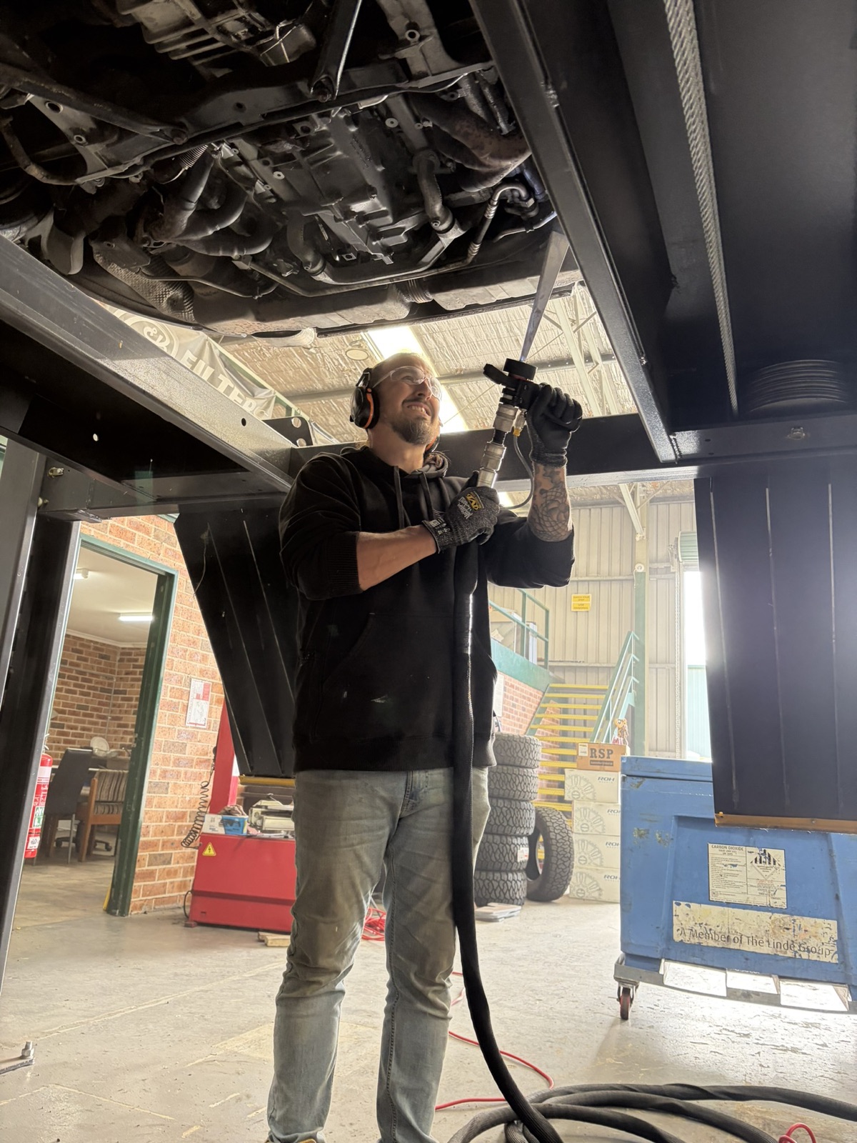 Operator with hearing protection working the blast nozzle under the car